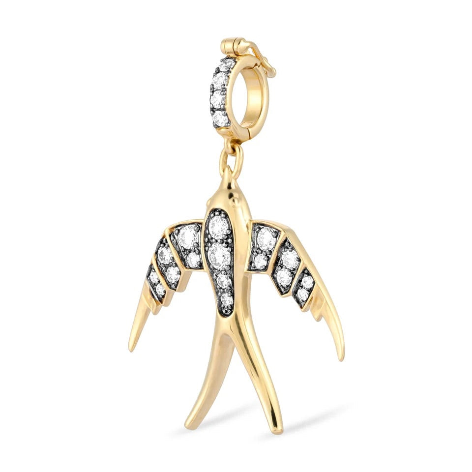 A gold bird charm pendant with clear gemstones set along its wings and a matching gemstone-covered bail, shown on a plain white background.
