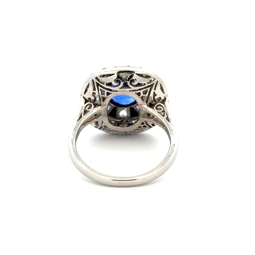A silver filigree ring featuring a central round-cut blue gemstone and a smaller clear stone set within an ornate openwork top, shown on a plain white background.