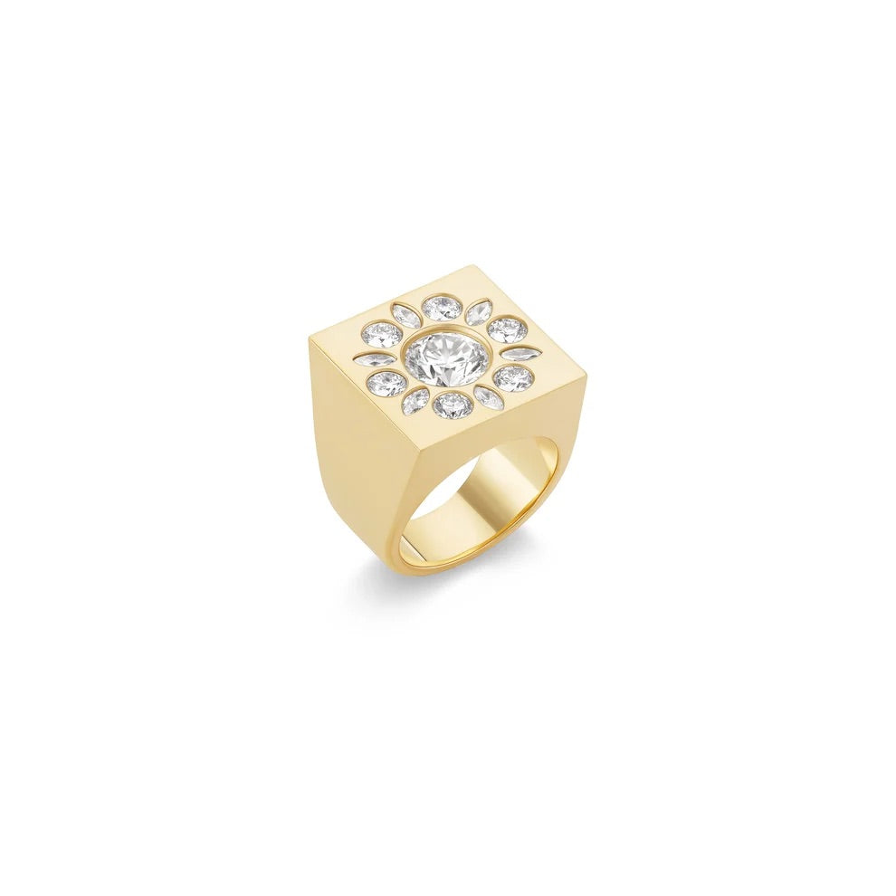 A yellow gold signet ring featuring a square face adorned with a halo of clear gemstones around a central round stone, set against a plain white background.