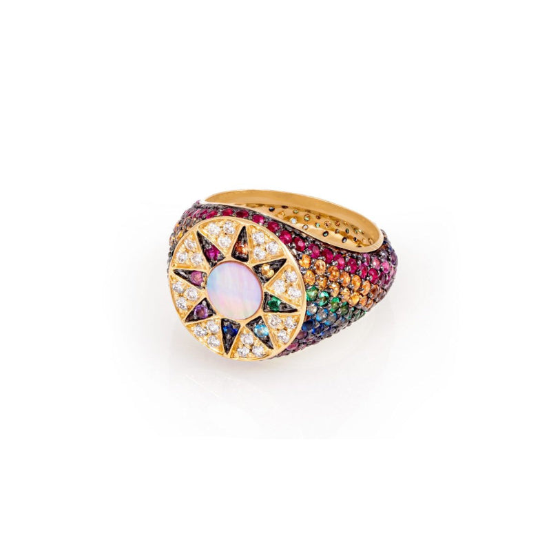 A gold signet ring featuring a central iridescent opal surrounded by star-shaped gold and diamond pavé settings, with a band encrusted with multicolored gemstones, shown on a white background.