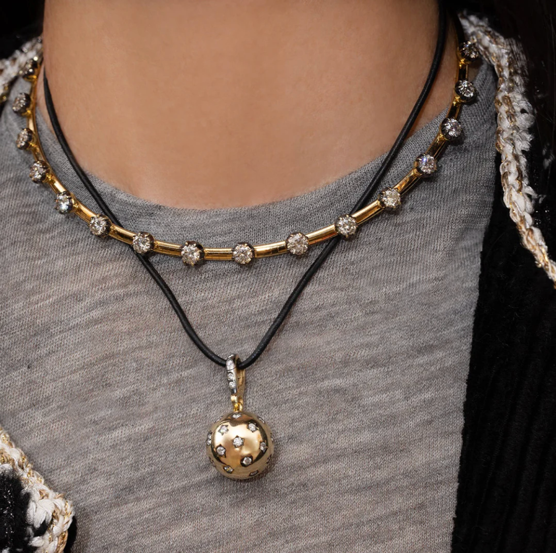 Close-up of a gold necklace with a pendant on a person wearing a gray top.