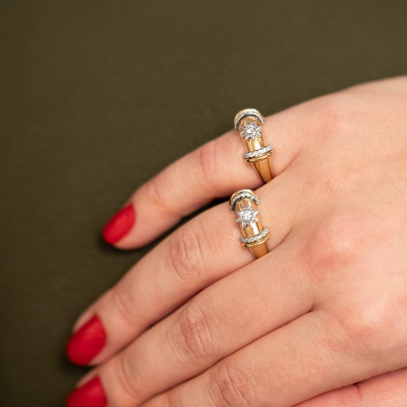 Hand wearing two gold rings with diamonds on a brown background