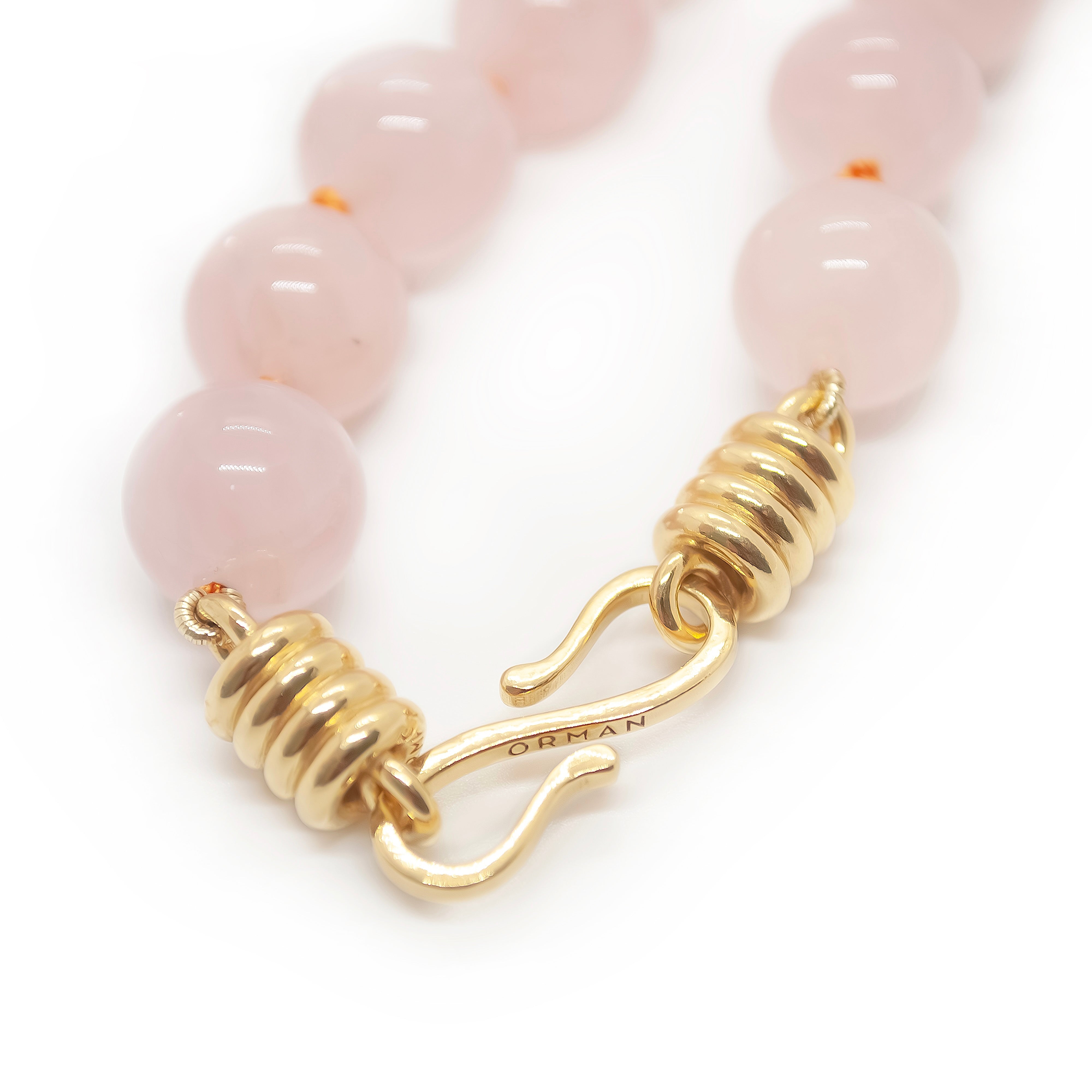 Close-up of a bracelet with pink beads and gold clasp on a white background