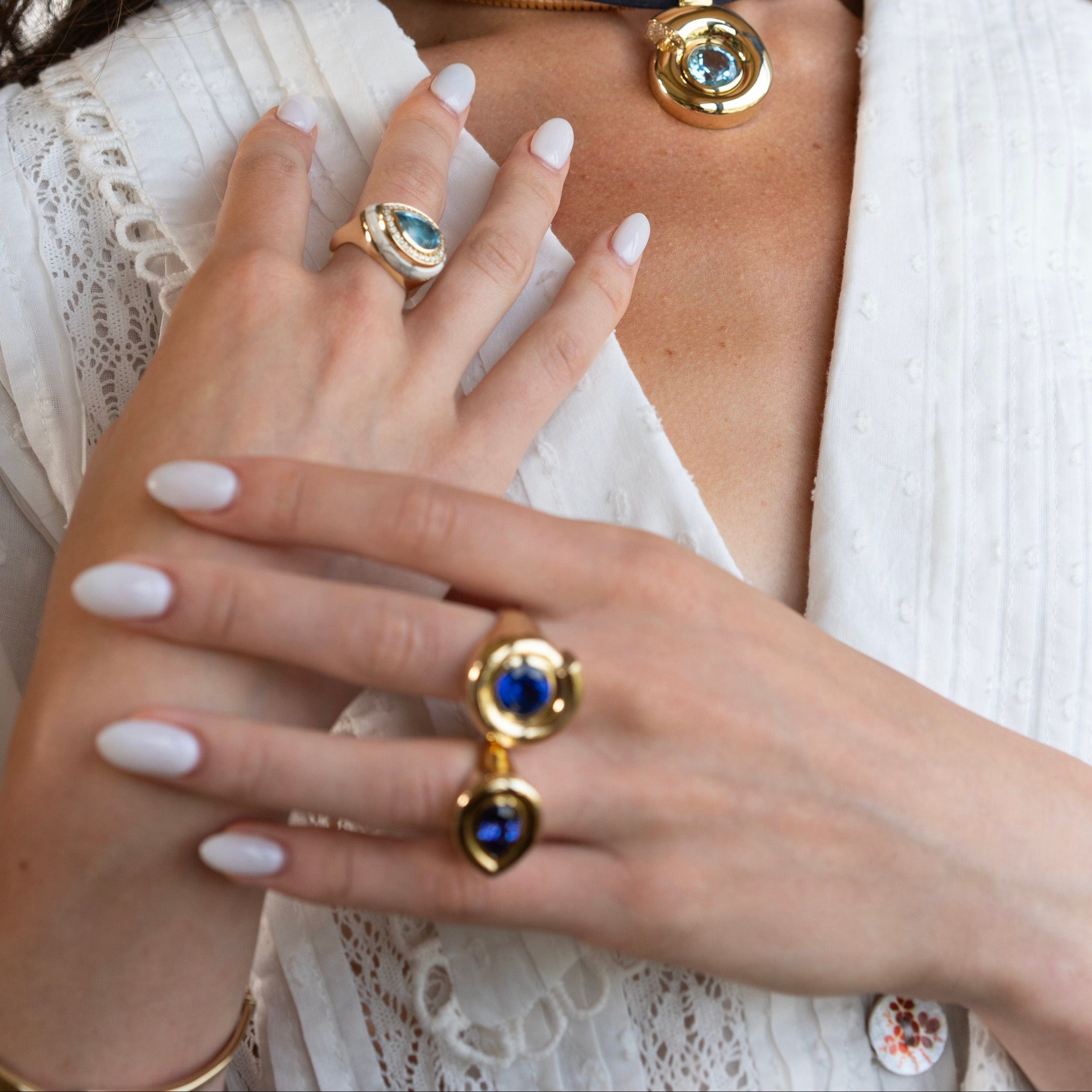 Close-up of a person wearing a gold necklace and rings with a white garment.