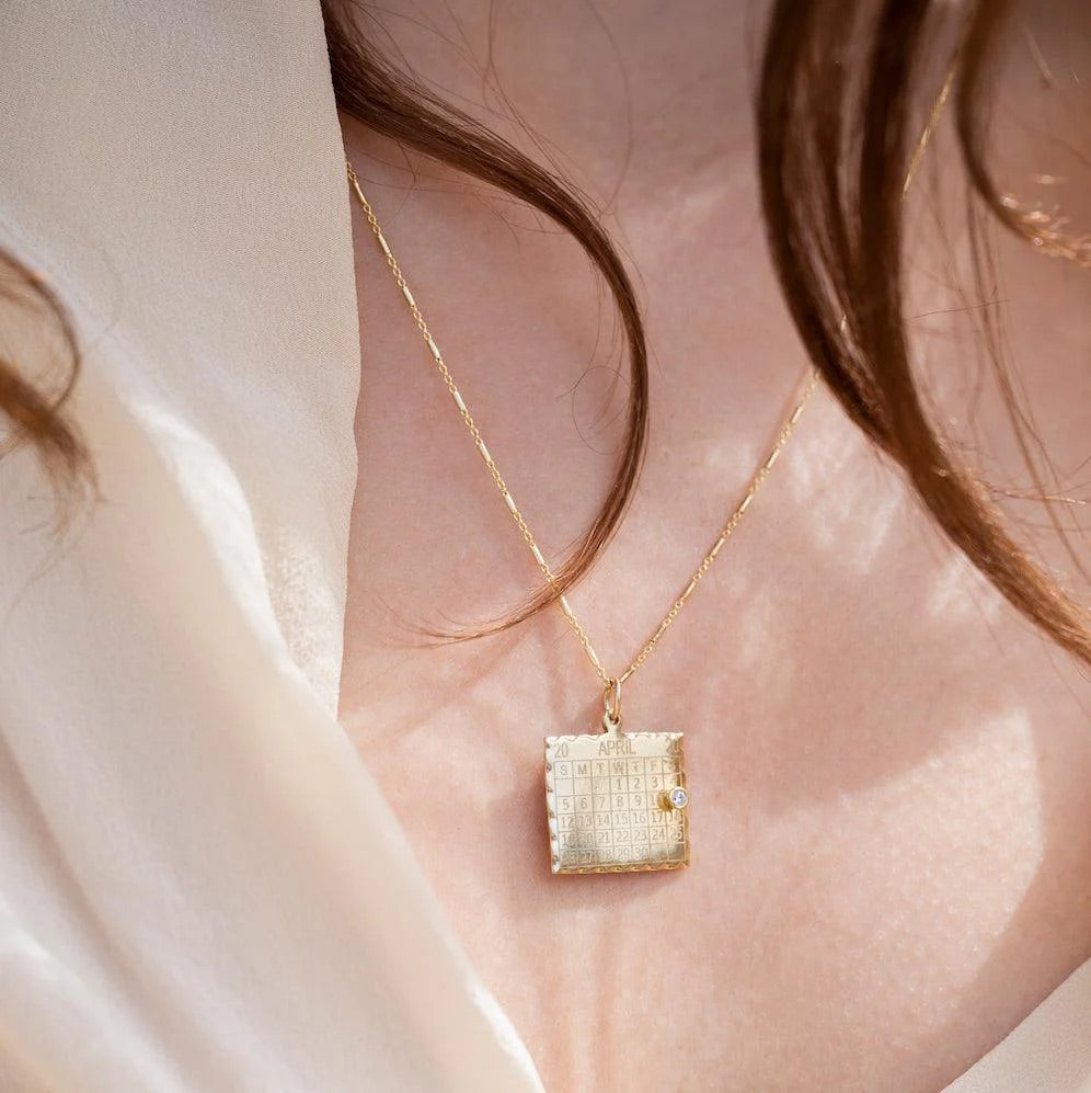 Gold necklace with a textured pendant on a person wearing a white blouse.