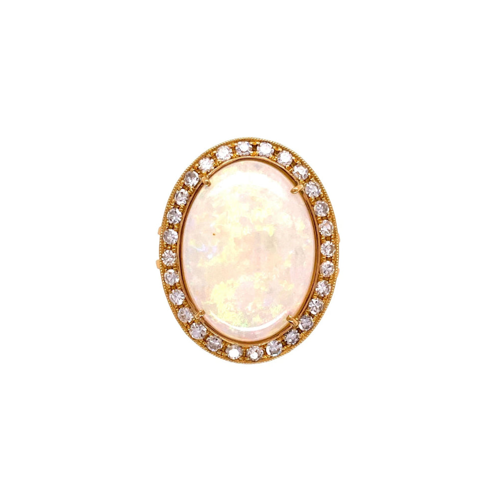 An oval yellow gold ring featuring a large, iridescent white opal cabochon in the center, surrounded by a halo of small clear round-cut diamonds on a white background.