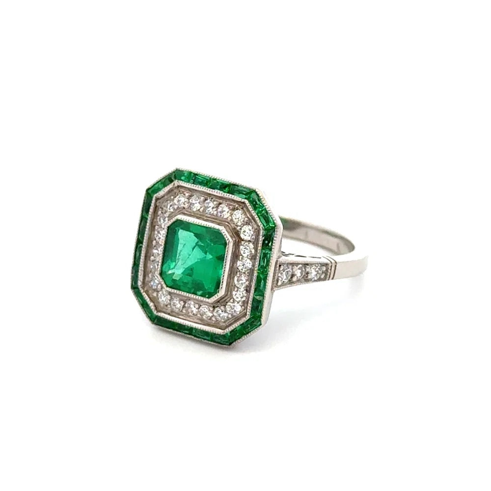 An octagonal emerald-cut emerald ring featuring a central green emerald, surrounded by a double halo of small clear diamonds in white gold, and a border of larger green diamonds, set on a polished white gold band.