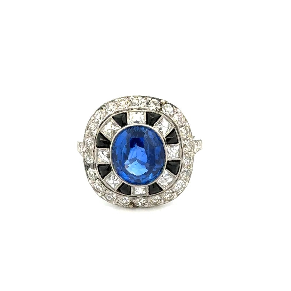 A vintage-style Art Deco ring featuring a round blue sapphire center stone surrounded by black and white diamonds in a geometric setting, on a plain white background.