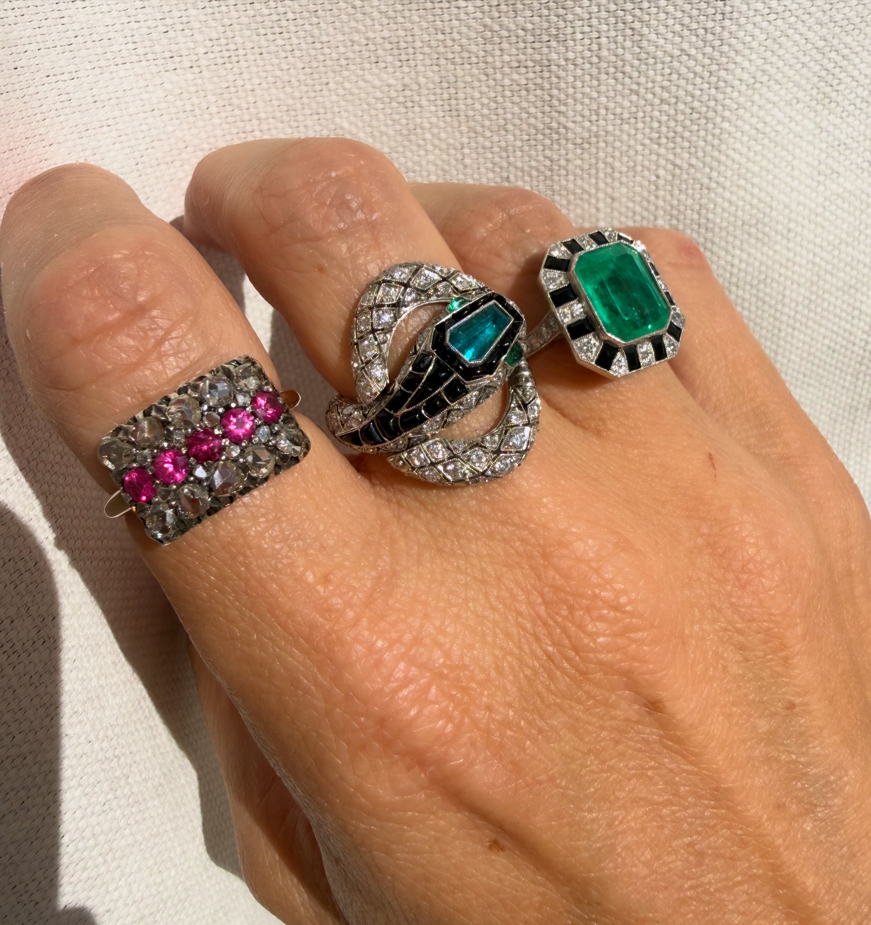 Three ornate rings with gemstones on a hand against a neutral background