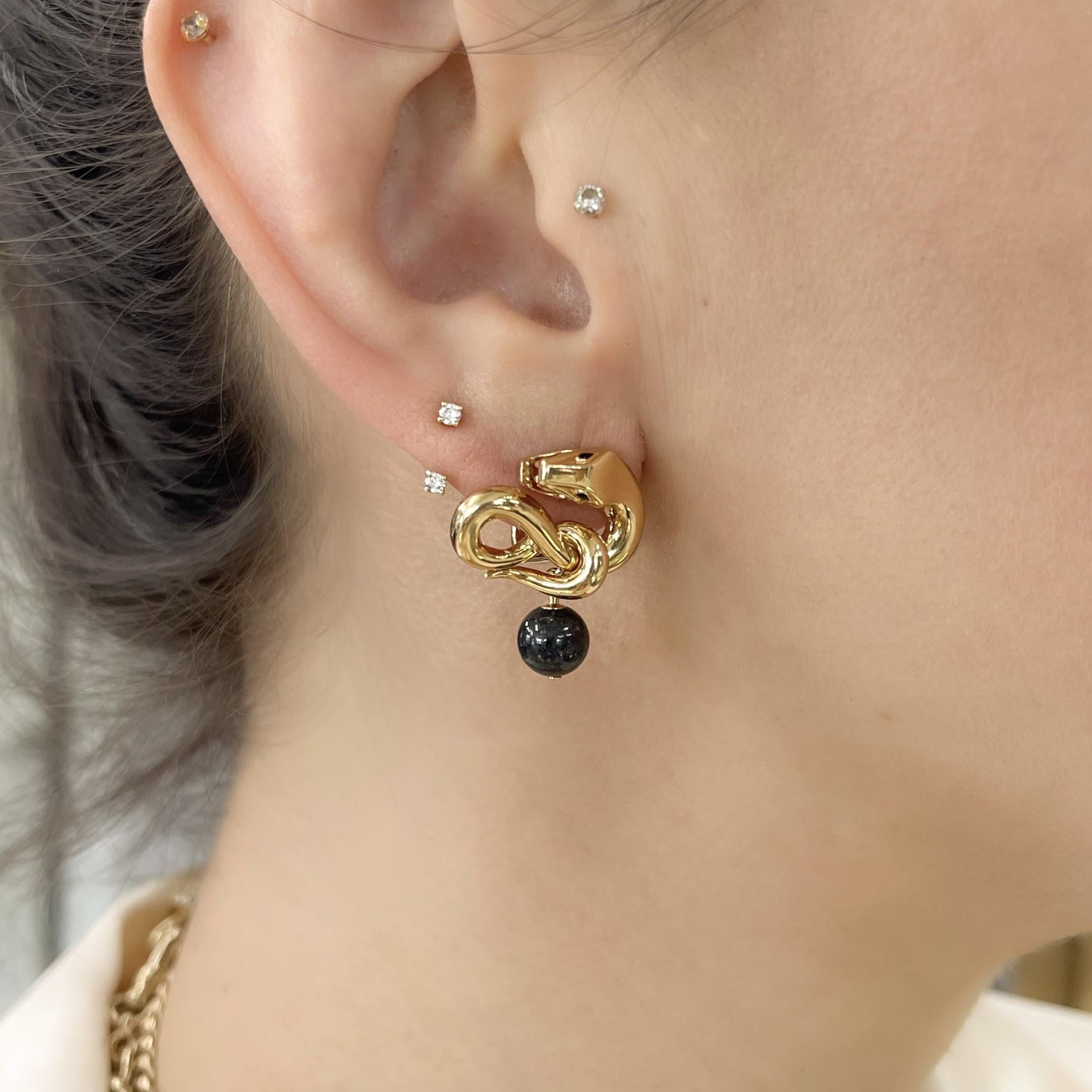 Close-up of an ear with gold hoop earrings featuring a black gemstone.