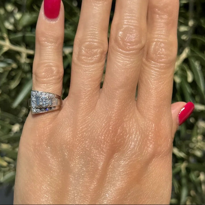 Hand with red nail polish wearing a silver ring against a green leafy background