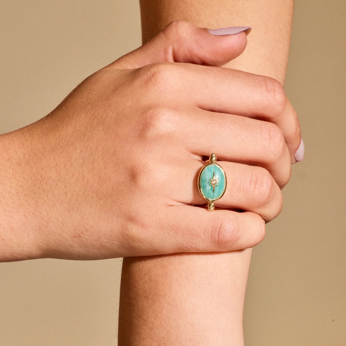 A close-up of a person's hand and forearm wearing a gold ring with an oval turquoise-colored stone featuring a small central gold star.