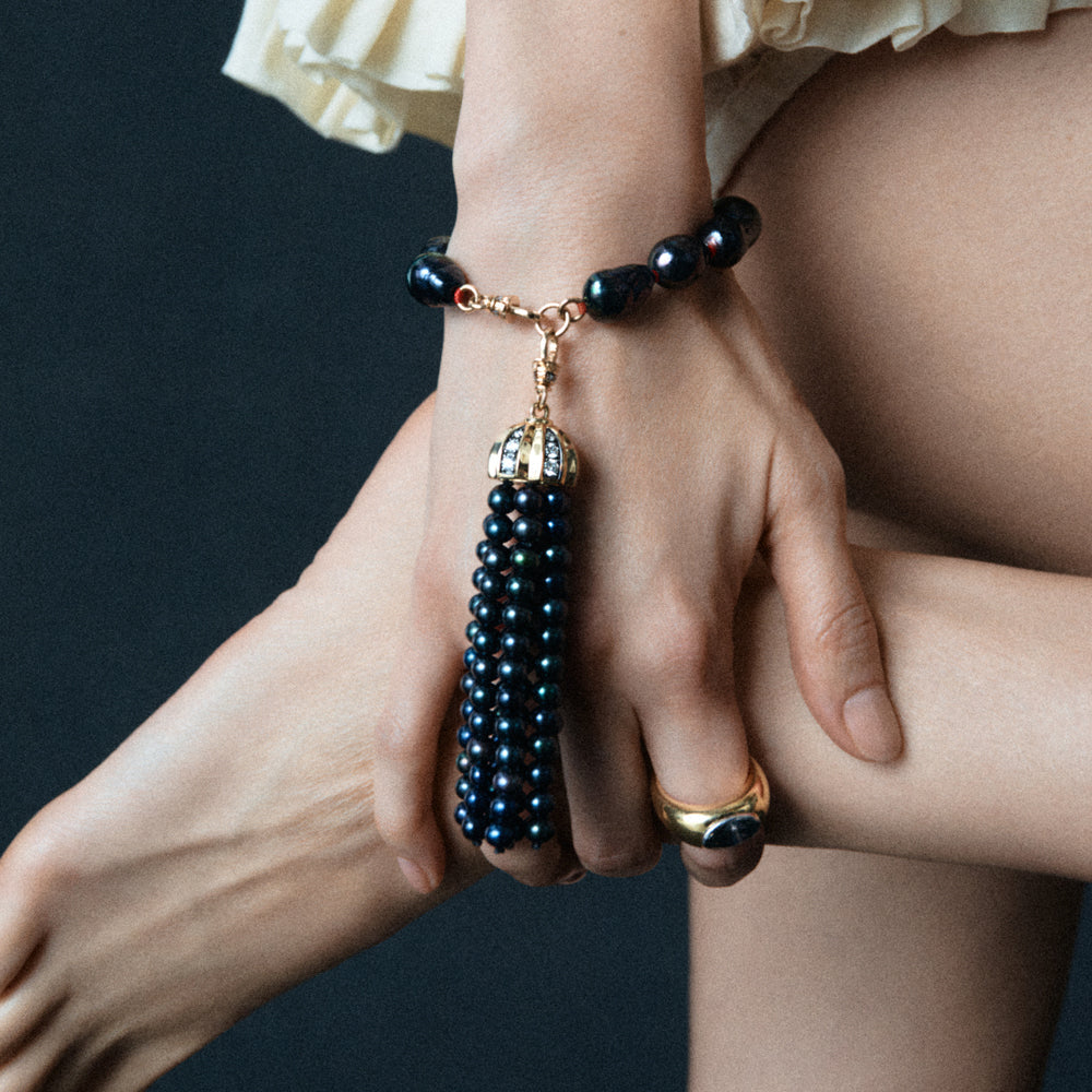 Person wearing a black beaded bracelet with a gold charm on a dark background