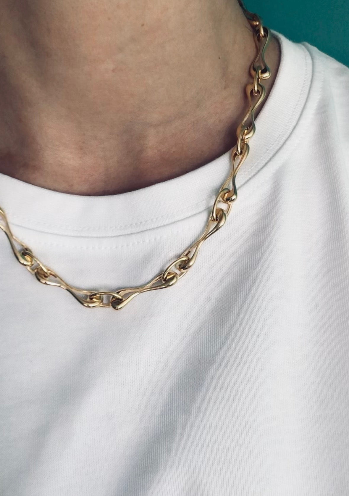 Gold chain necklace worn by a person on a white shirt