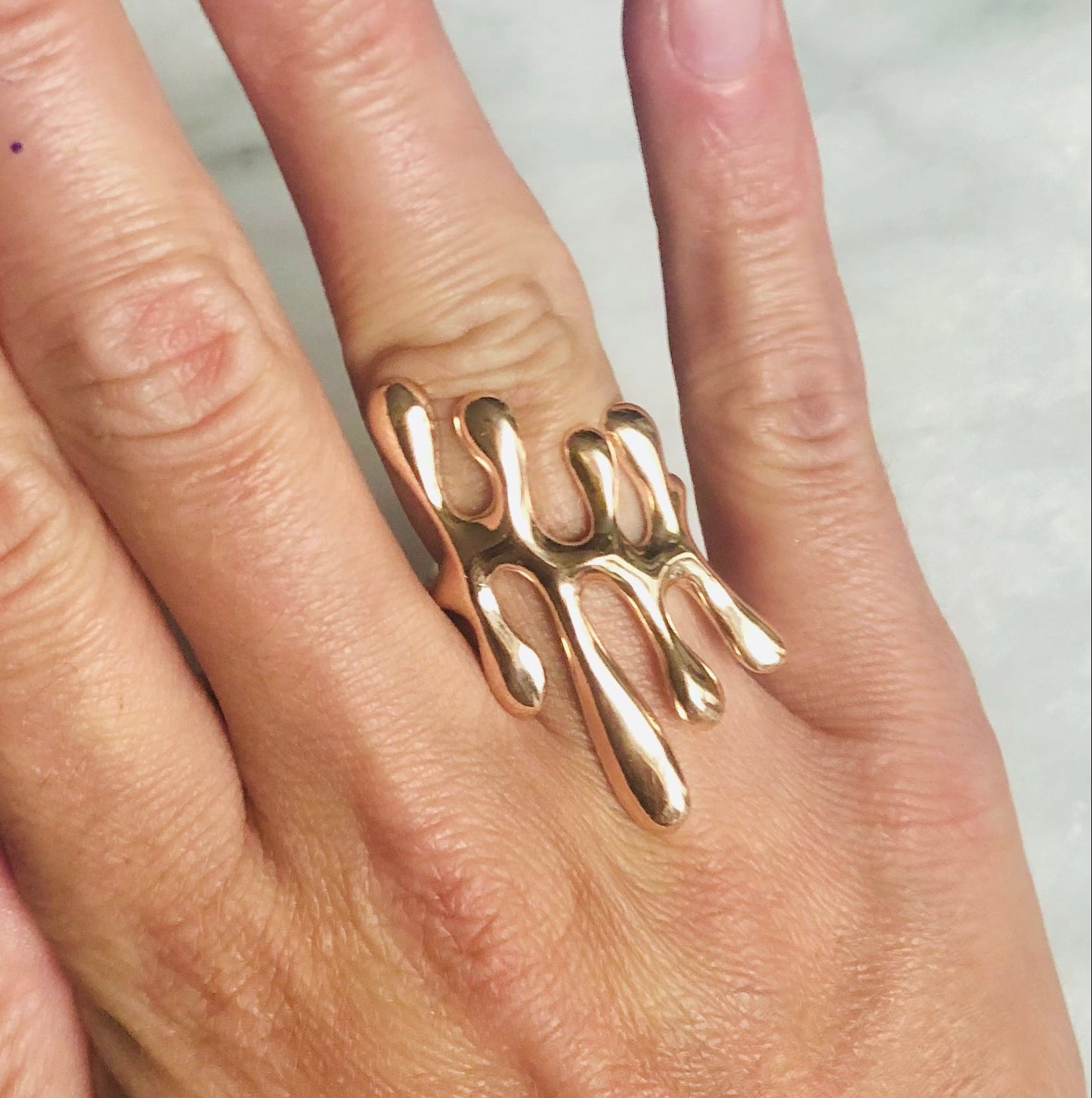 Hand wearing a gold ring with a unique design on a light background