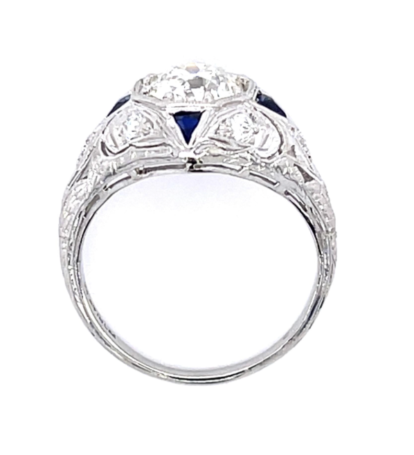 An Art Deco style silver ring featuring a large clear round center stone, smaller clear stones, and dark blue triangular accent stones on a white background.