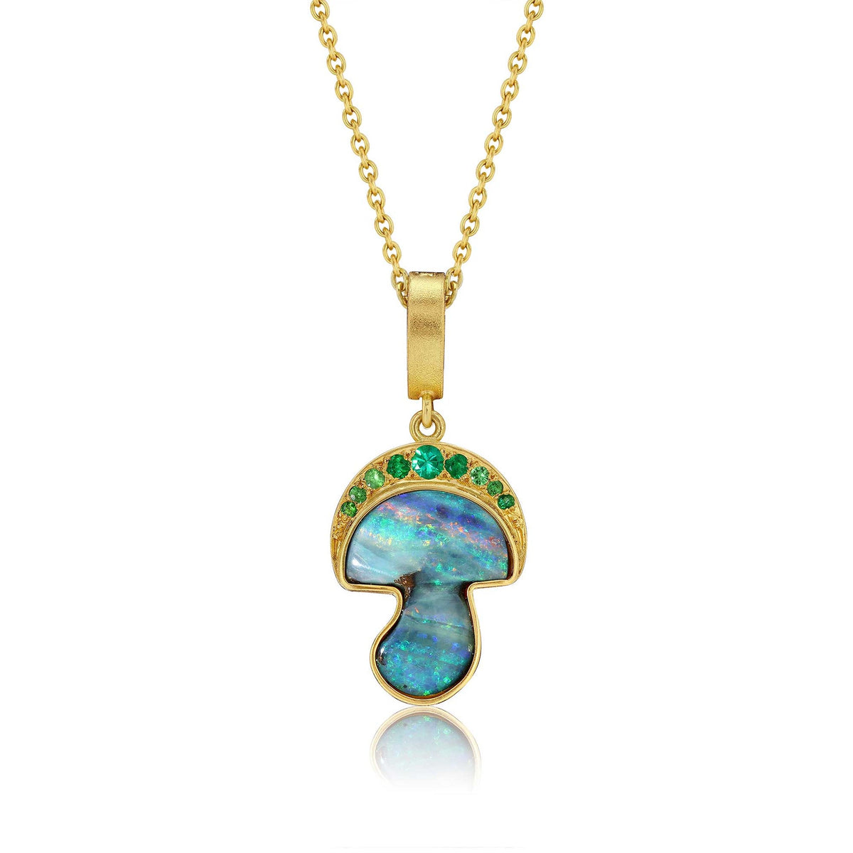 A gold mushroom-shaped pendant necklace featuring a blue and green iridescent opal inlay, accented with small green gemstones along the cap edge, shown on a white background with a soft reflection.