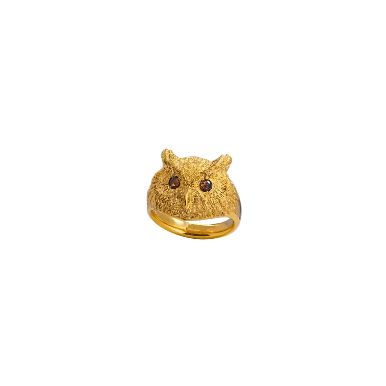 A gold owl ring with textured feather-like detailing and dark eyes, displayed on a white cylindrical pedestal against a light gray background.