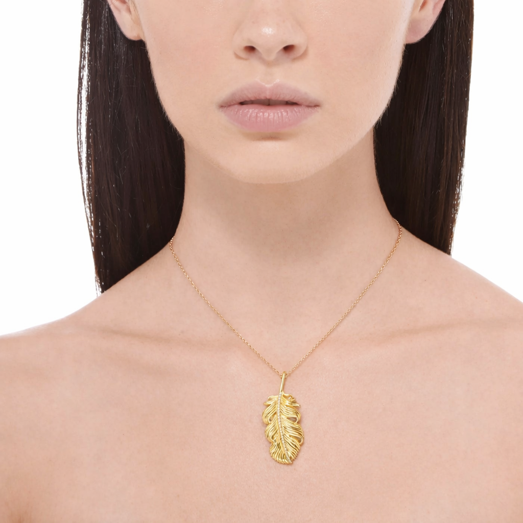 Woman wearing a gold necklace with a leaf pendant on a white background