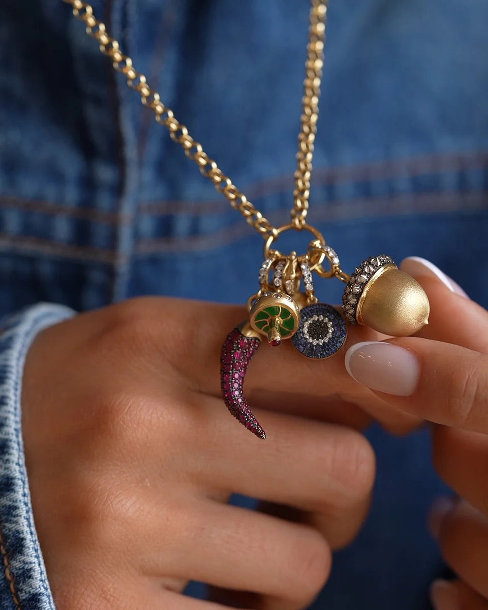 Gold necklace with various charms held by a hand against a blue denim background