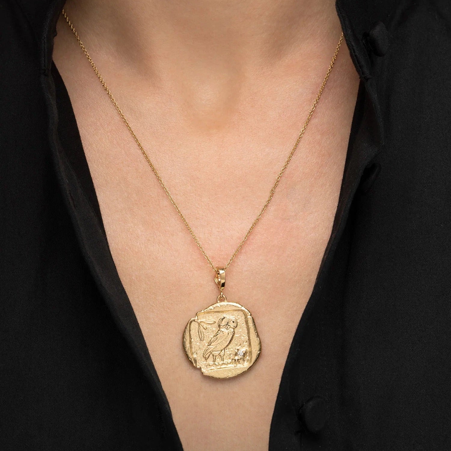 A close-up of a person wearing a delicate gold chain necklace with a textured, coin-like oval pendant featuring an engraved bird.