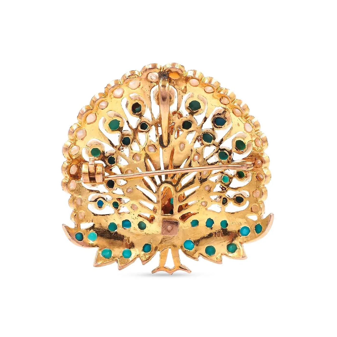 Gold peacock brooch with green and blue gemstones on a white background