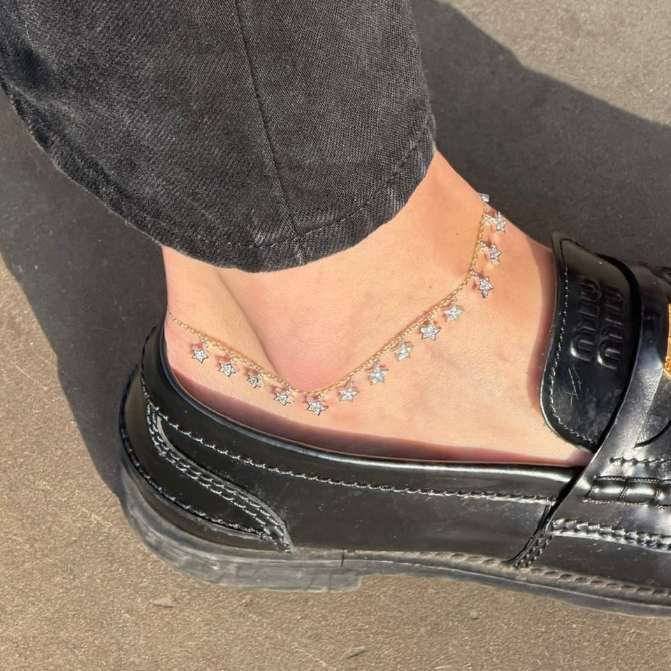 Black flat shoe worn with a diamond anklet on a concrete surface