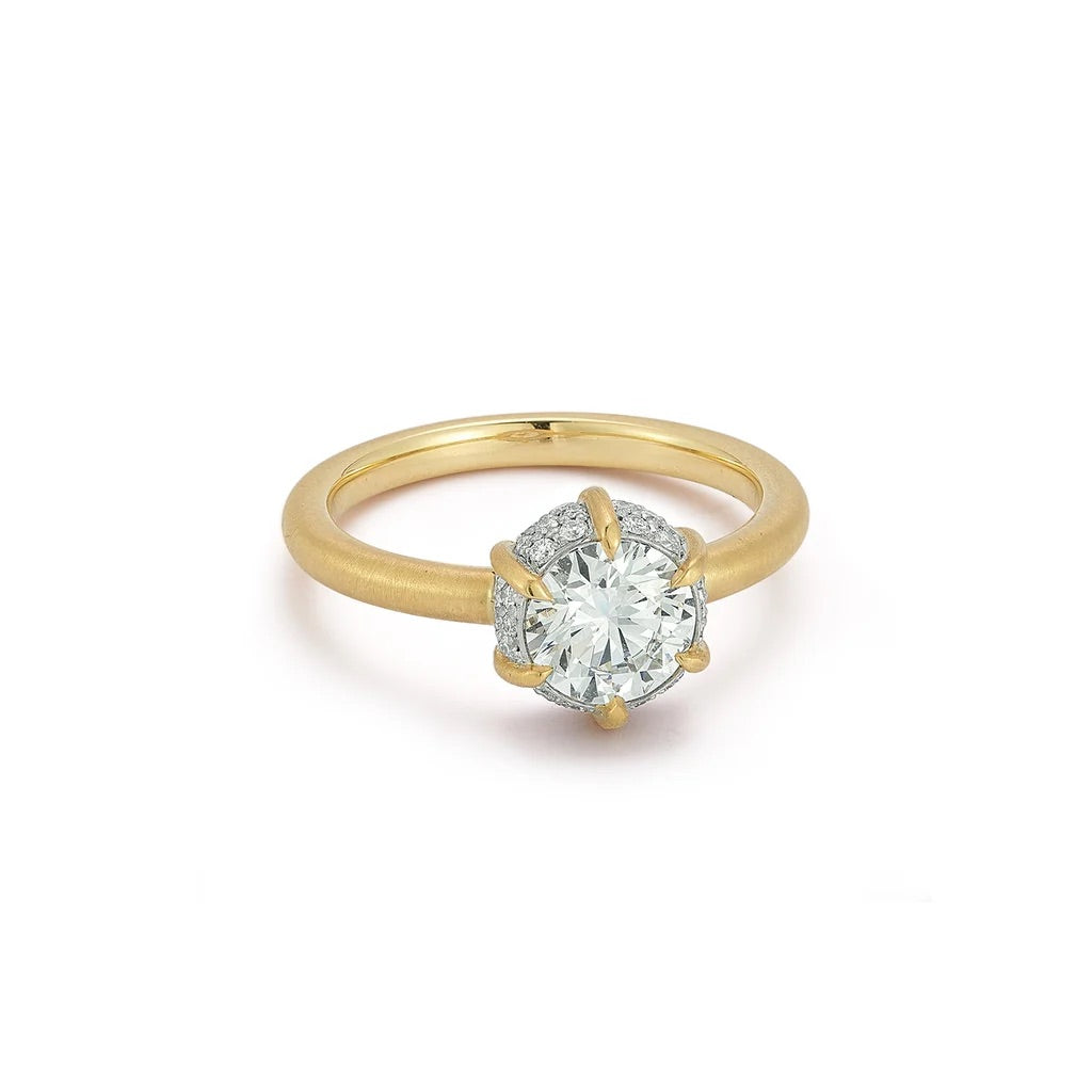 A yellow gold solitaire engagement ring featuring a round brilliant-cut center stone and a halo of smaller diamonds on a white background.