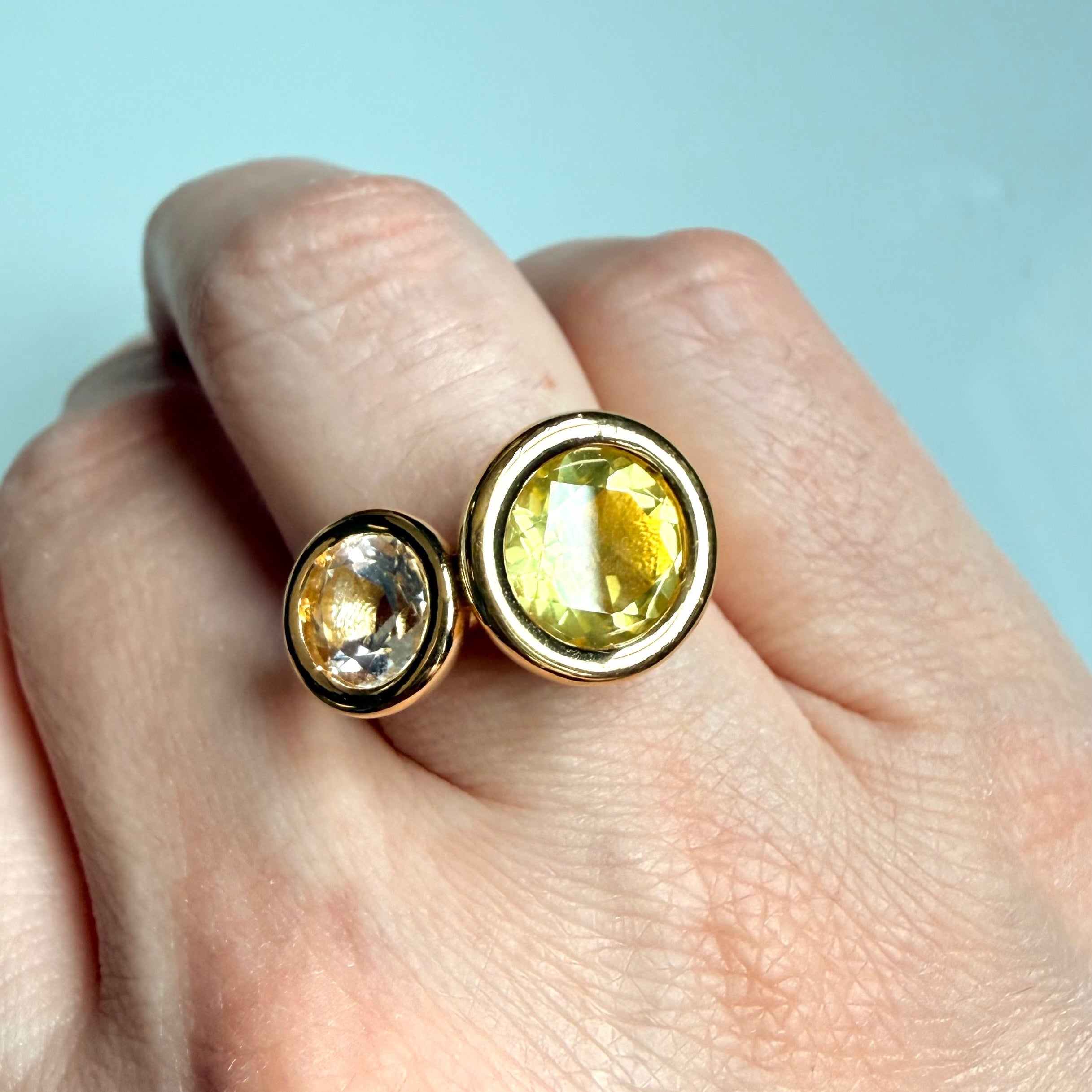 Gold ring with yellow gemstone on a hand against a light blue background