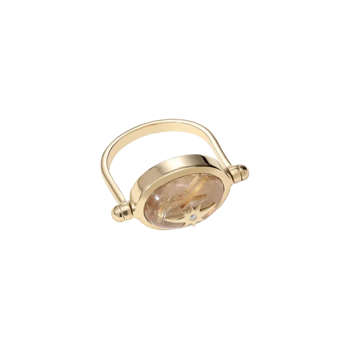 A gold-toned ring with a circular clear stone containing fine gold and light brown inclusions, accented by a small star-shaped detail and a tiny blue gemstone, set against a warm off-white background.