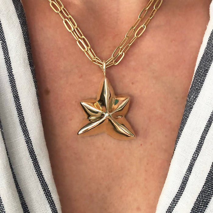 Gold star-shaped pendant necklace on a person wearing a striped garment.