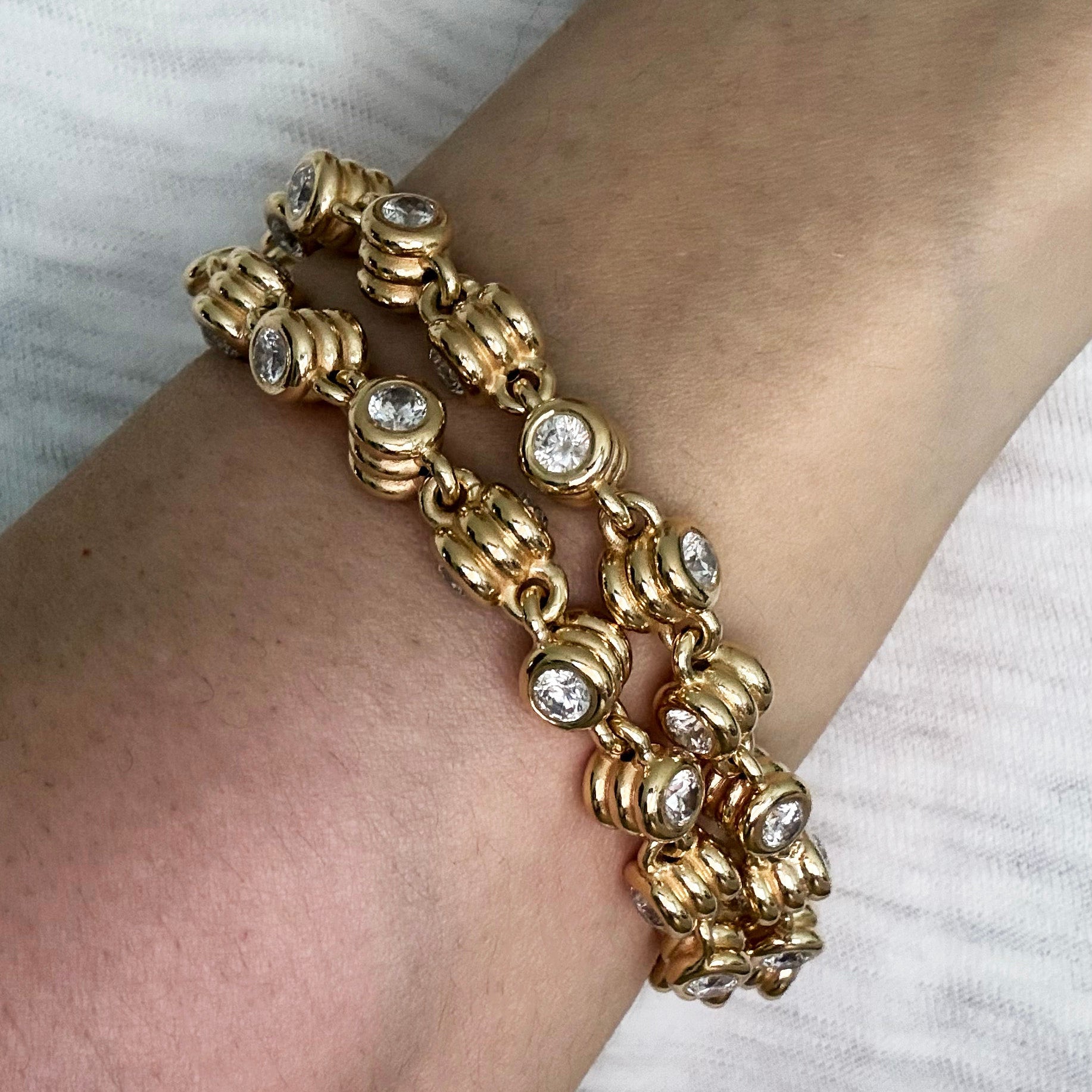 Gold bracelet with clear stones on a wrist against a white background