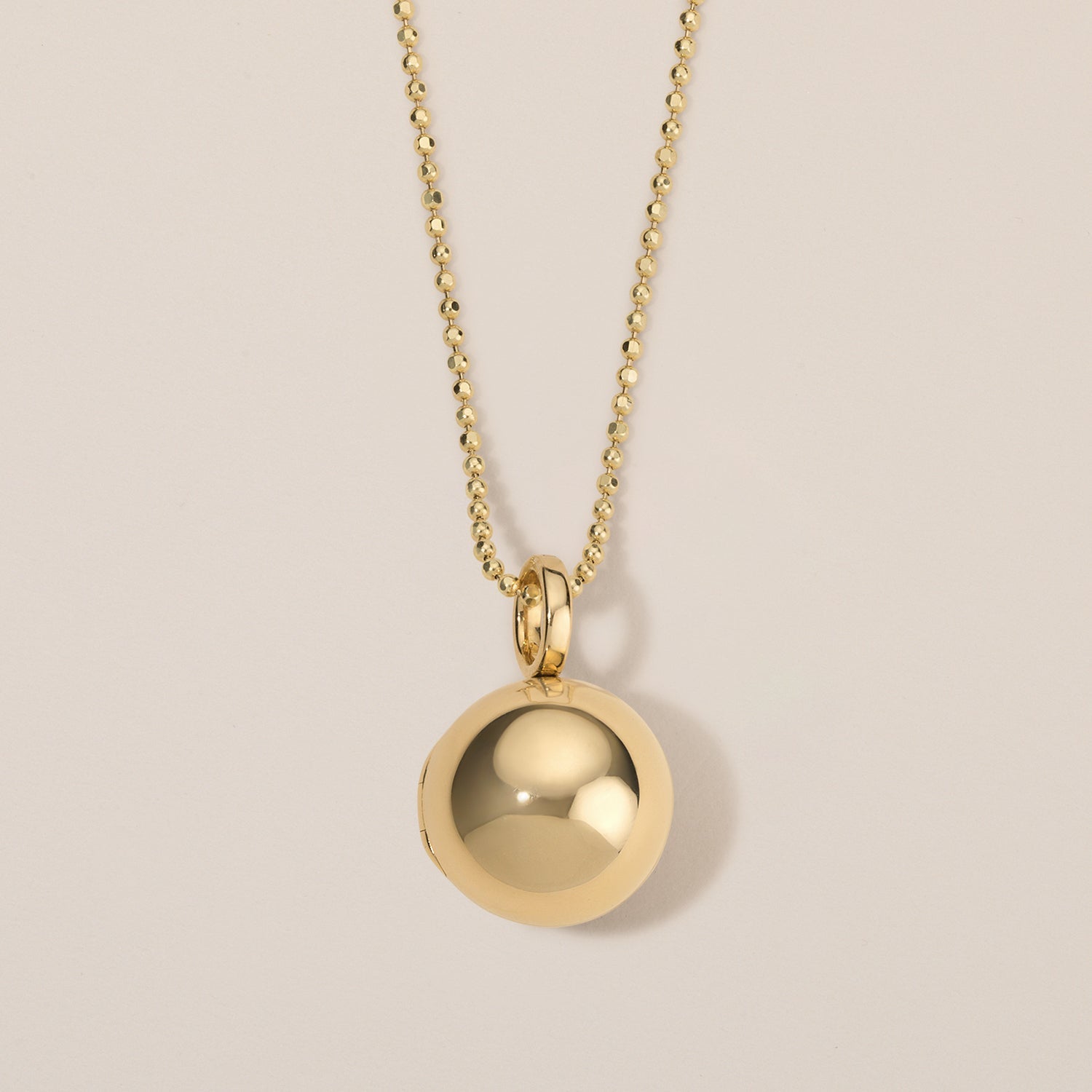 Gold necklace with a round pendant on a beige background
