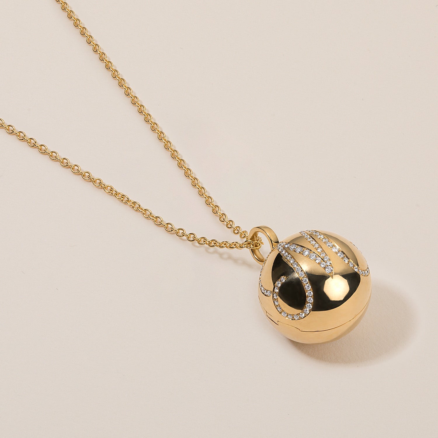 Gold necklace with a spherical pendant on a beige background