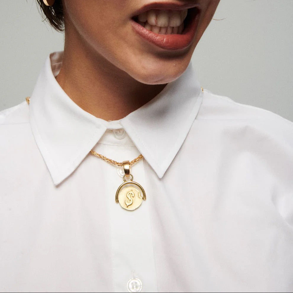 Person wearing a white shirt with gold jewelry on a gray background