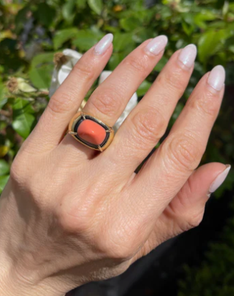 Hand wearing a ring with coral stone against a blurred green background