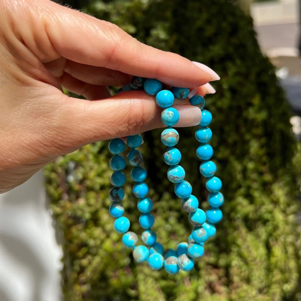 Hand holding a blue beaded necklace against a blurred green background