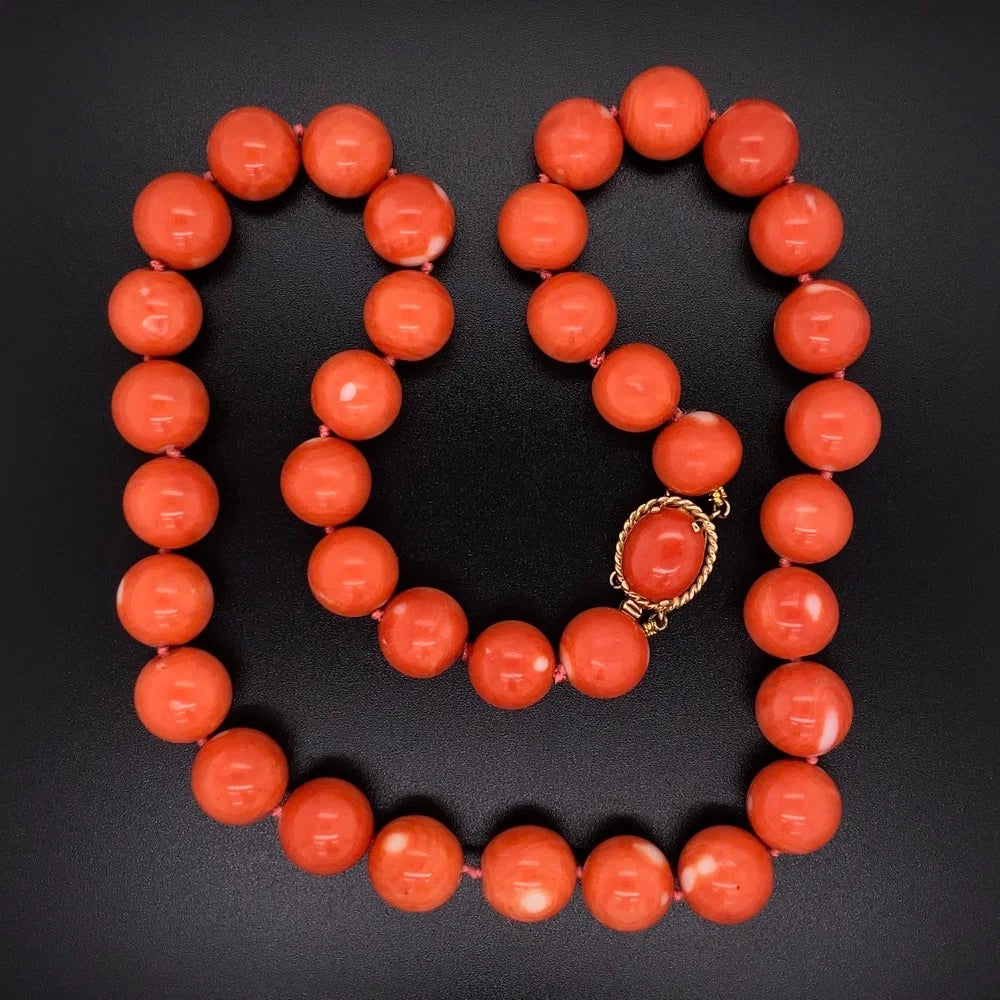 Coral bead necklace with a gold clasp on a black background