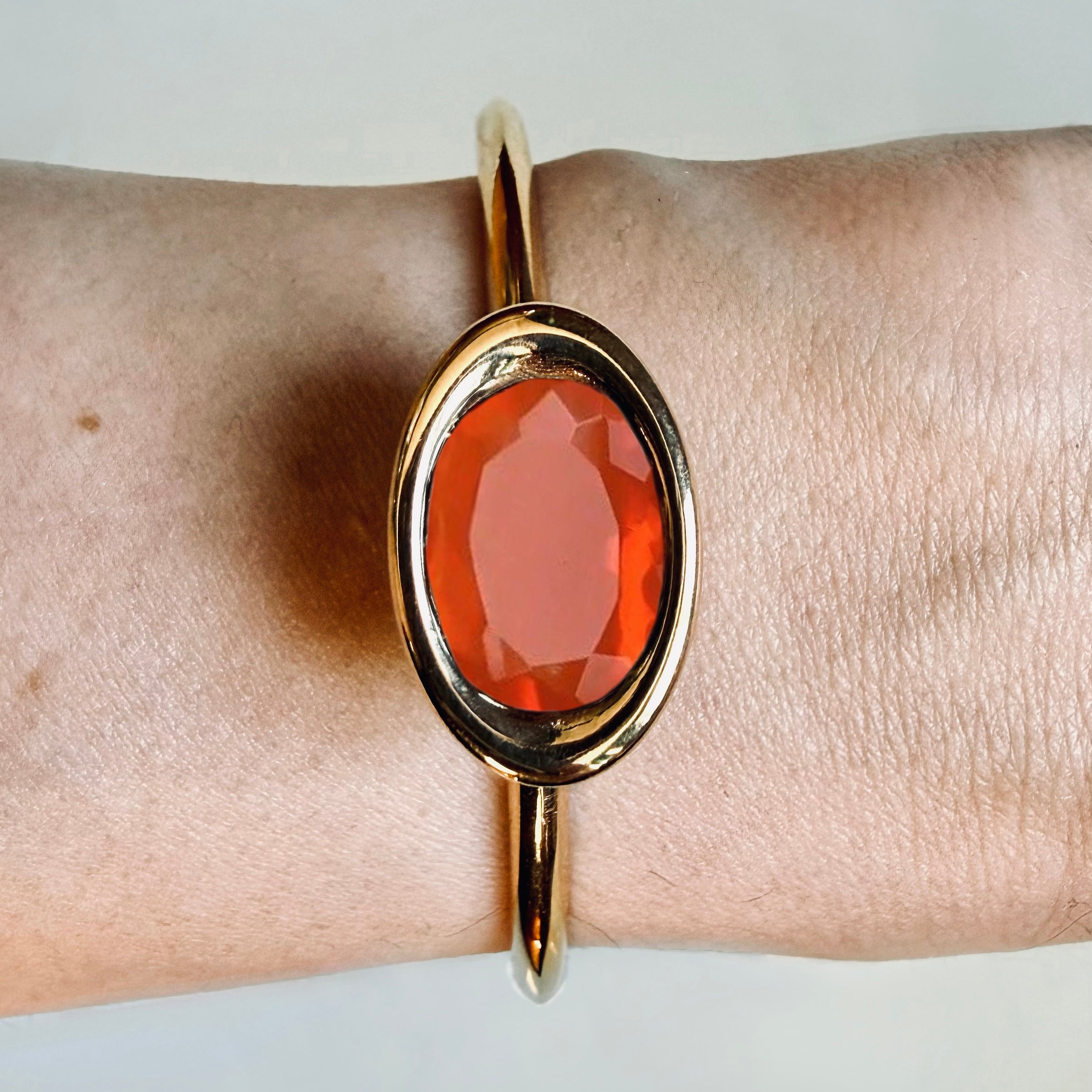 Gold bracelet with a red stone on a wrist against a light background