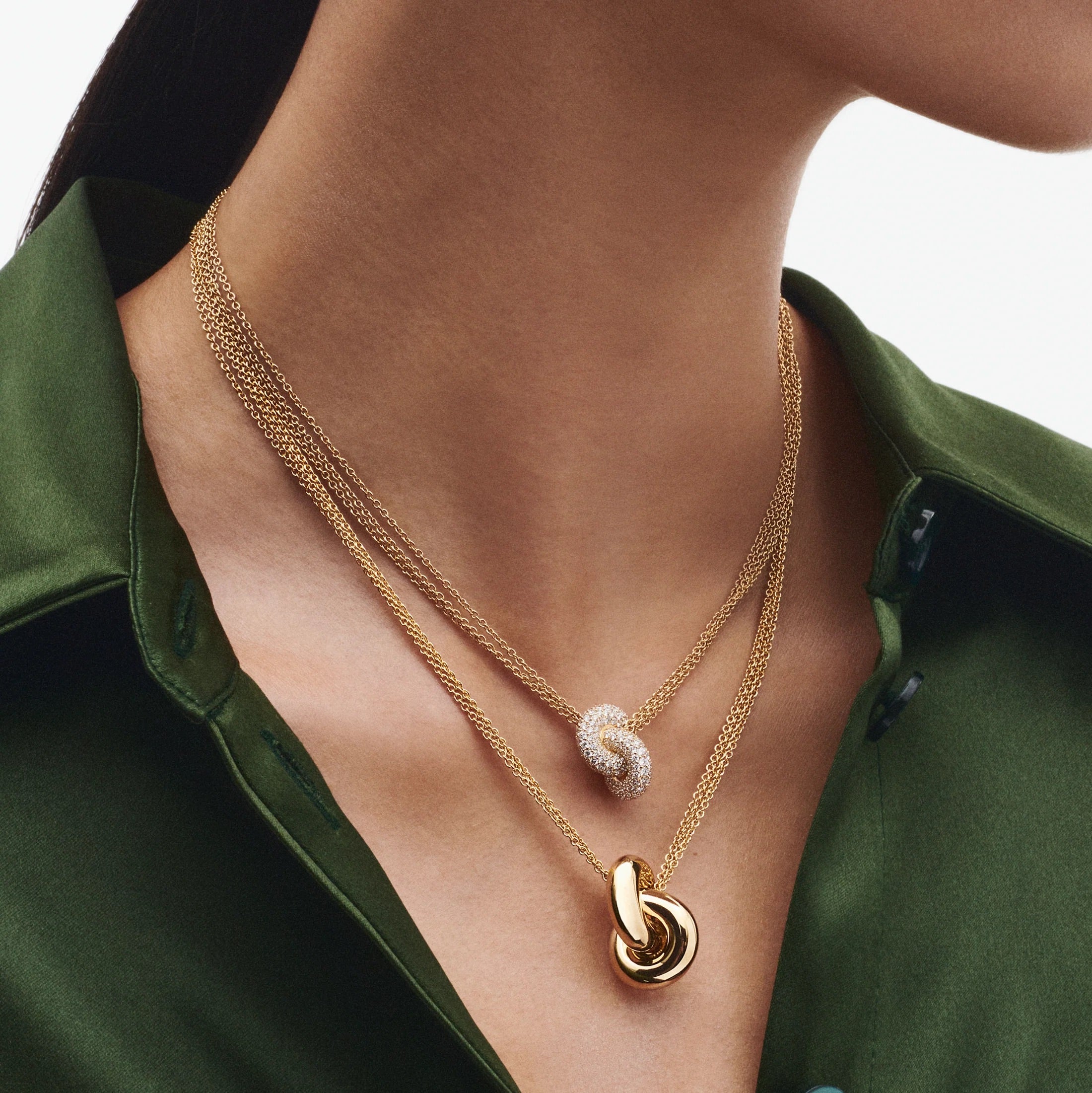 Two gold necklaces with pendants on a person wearing a green shirt.