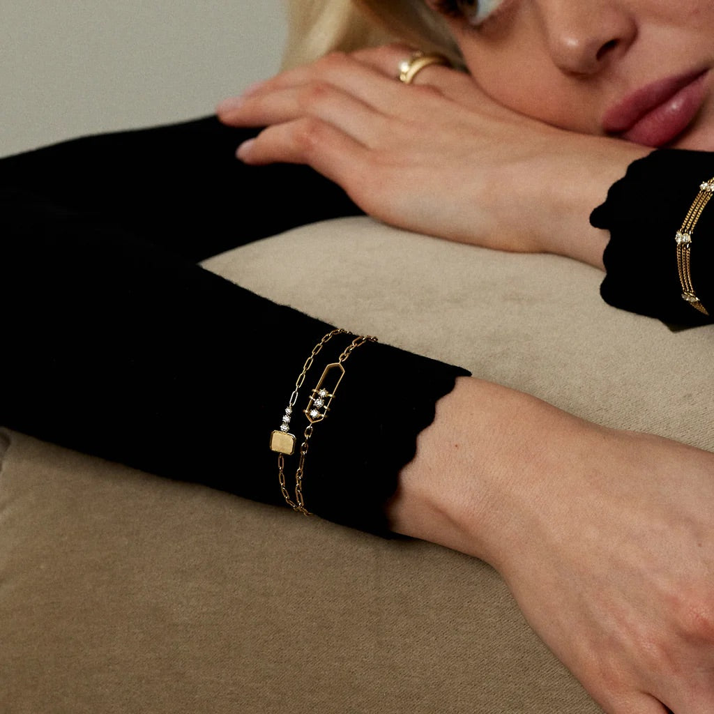 Person wearing gold bracelets on a beige surface