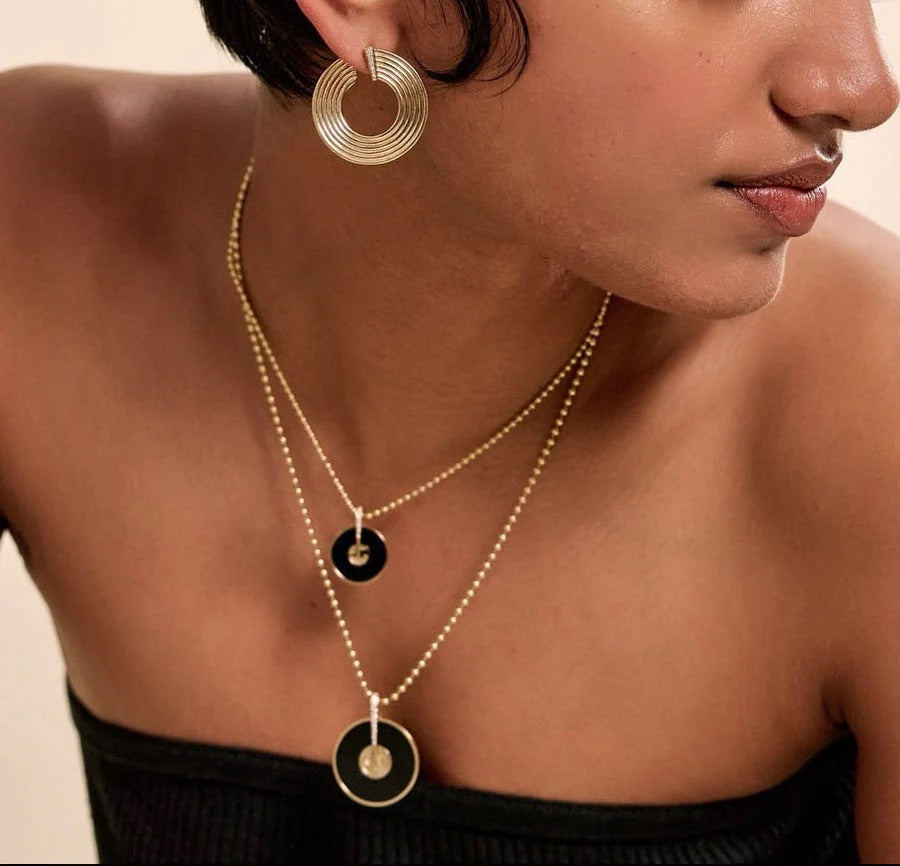Close-up of a woman wearing gold hoop earrings and a necklace with black circular pendants.
