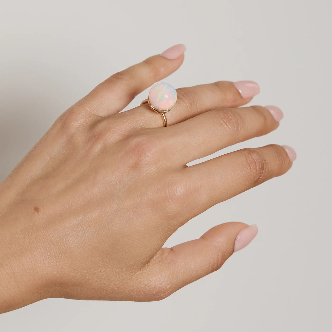 Hand wearing a ring with an opal stone on a neutral background