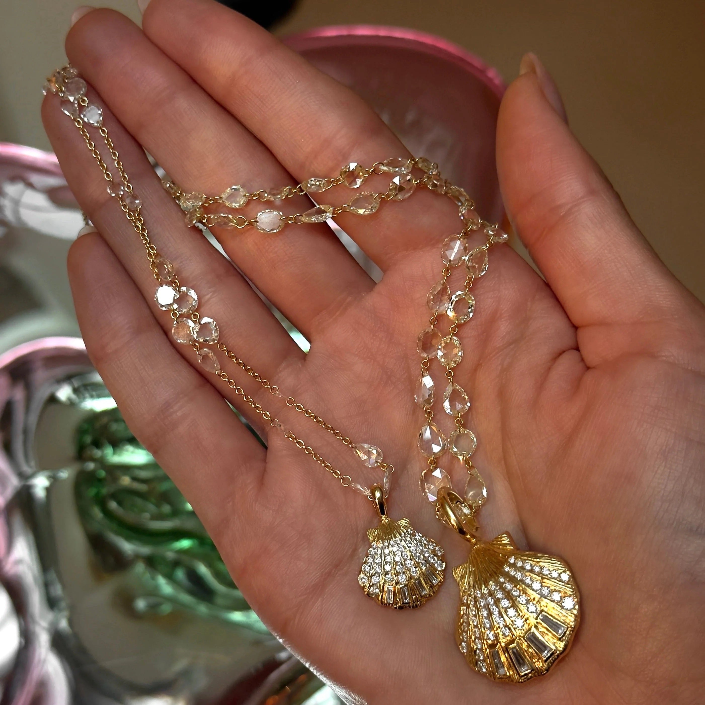 Hand holding a gold necklace with shell-shaped pendants against a blurred background