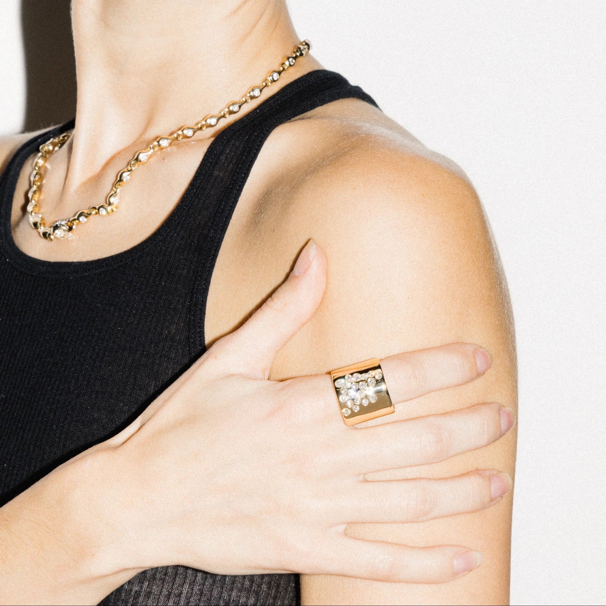 Person wearing a gold chain necklace and ring on a plain background