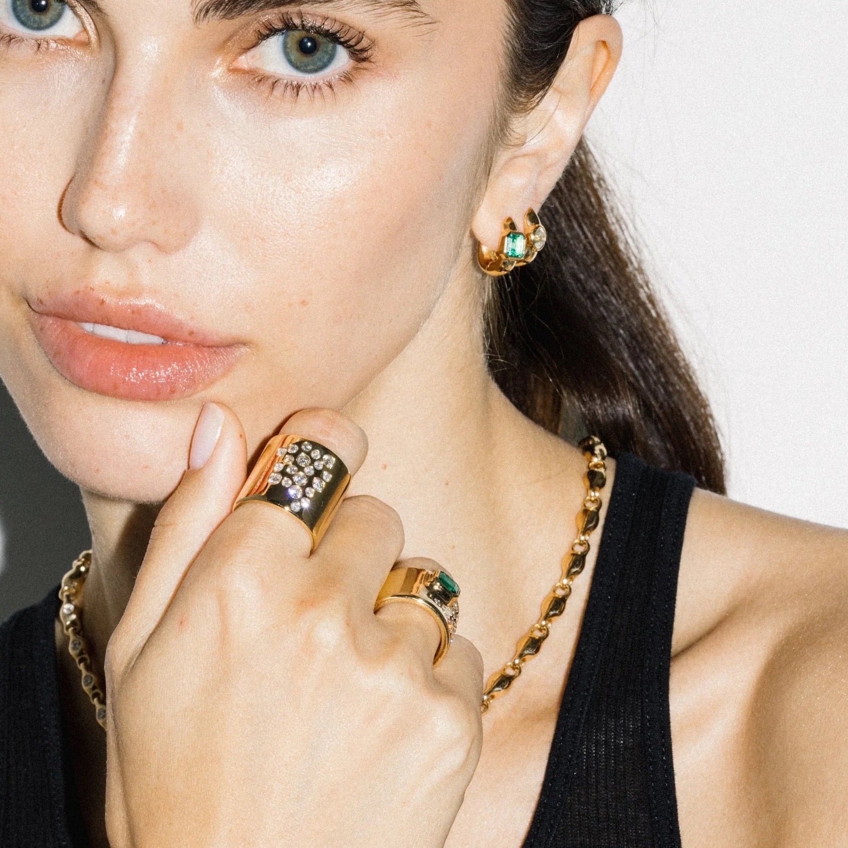 Close-up of a woman wearing gold jewelry with green gemstones against a neutral background