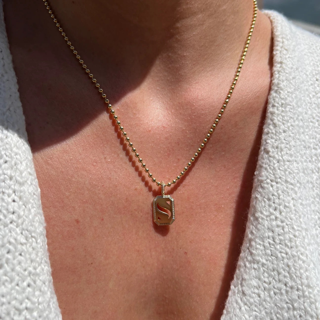 Gold necklace with a 'S' pendant on a person wearing a white textured garment.