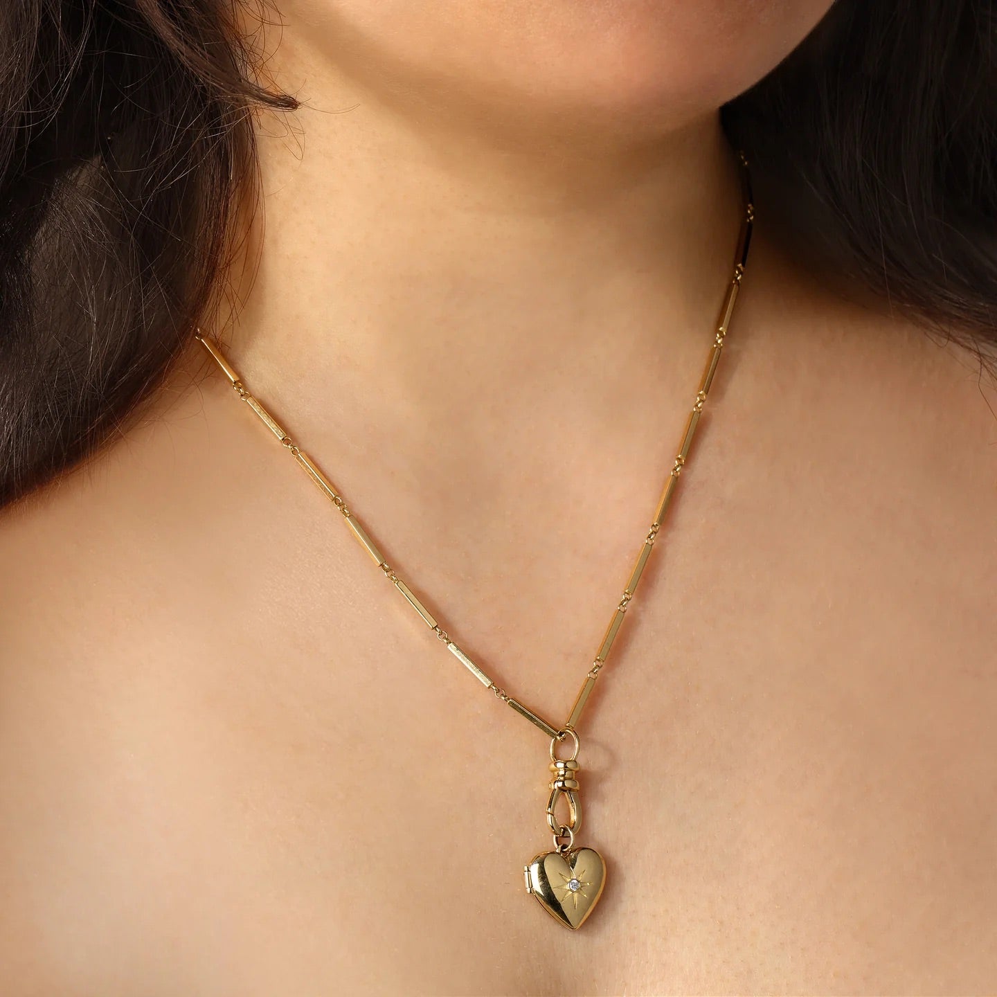 Gold necklace with a heart pendant worn by a person, on a soft beige background.