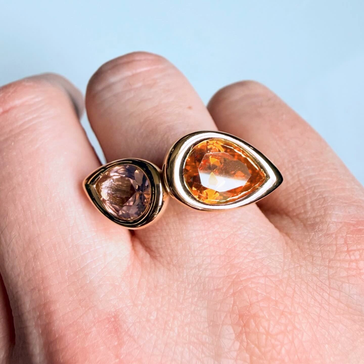 Two gold rings with pear-shaped gemstones on a hand against a light blue background