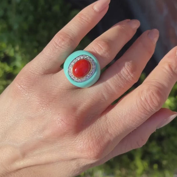 Hand wearing a turquoise ring with a red gemstone against a blurred green background